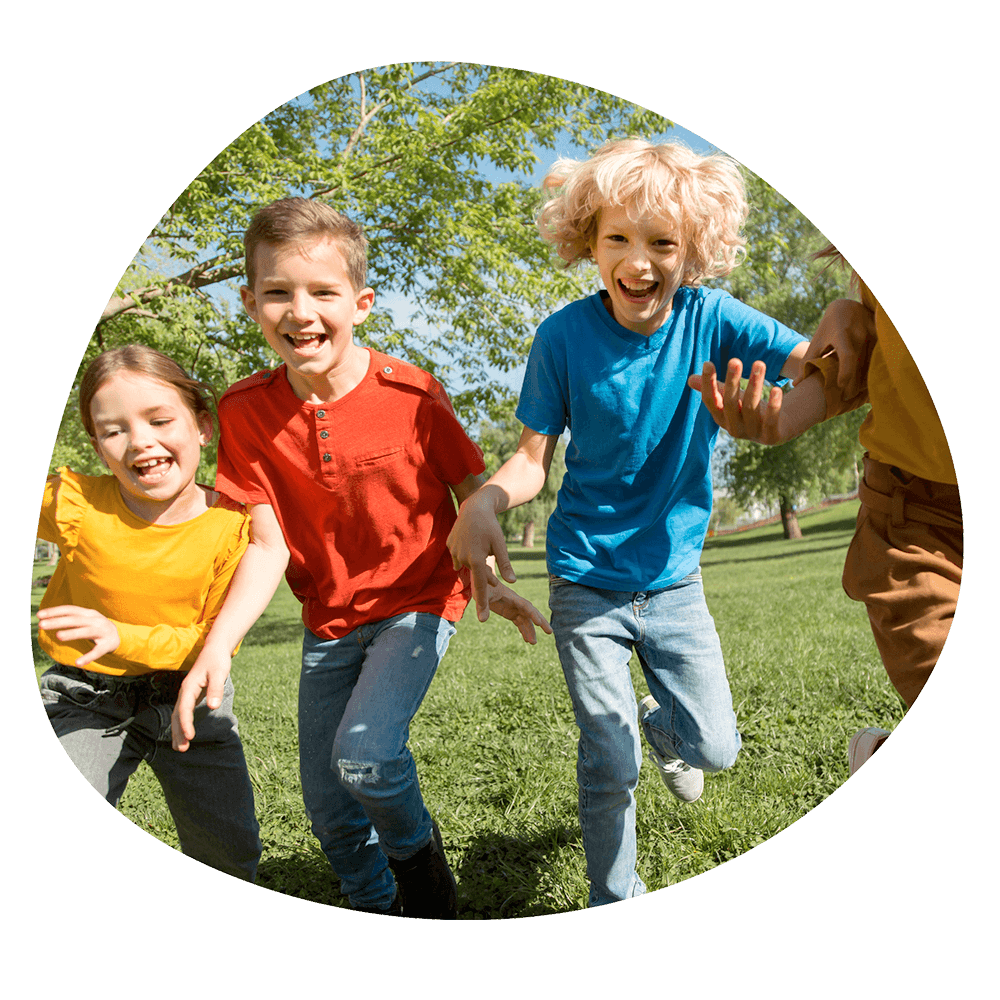 Tre bambini che corrono e ridono in un parco verde durante un'attività all'aperto del corso estivo Move Your Summer