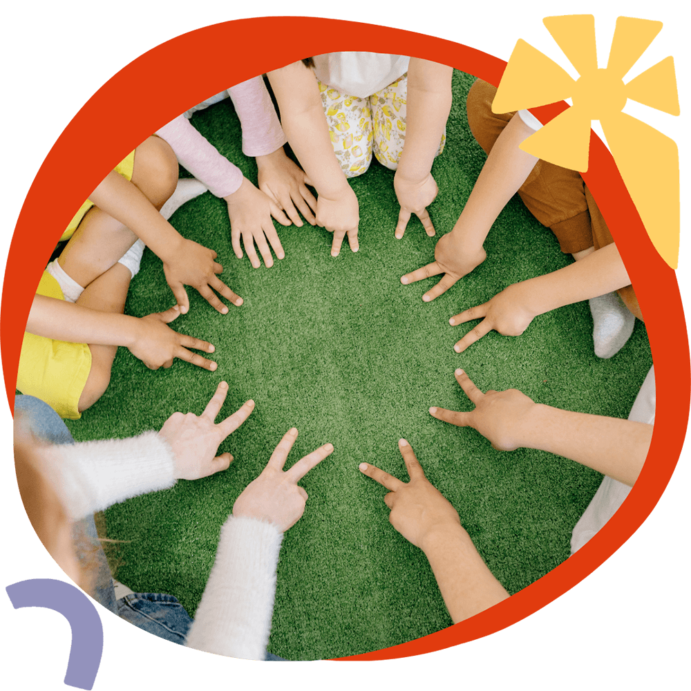 Un gruppo di bambini seduti in cerchio sull'erba con le mani al centro, durante un'attività CLIL del corso estivo Move Your Summer