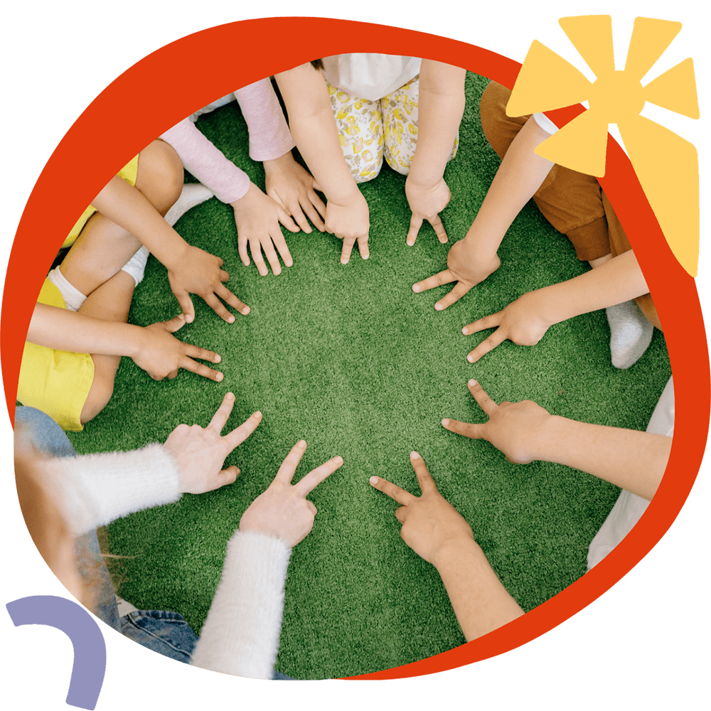 Attività 8 Un gruppo di bambini seduti in cerchio sull'erba con le mani al centro, durante un'attività CLIL del corso estivo Move Your Summer