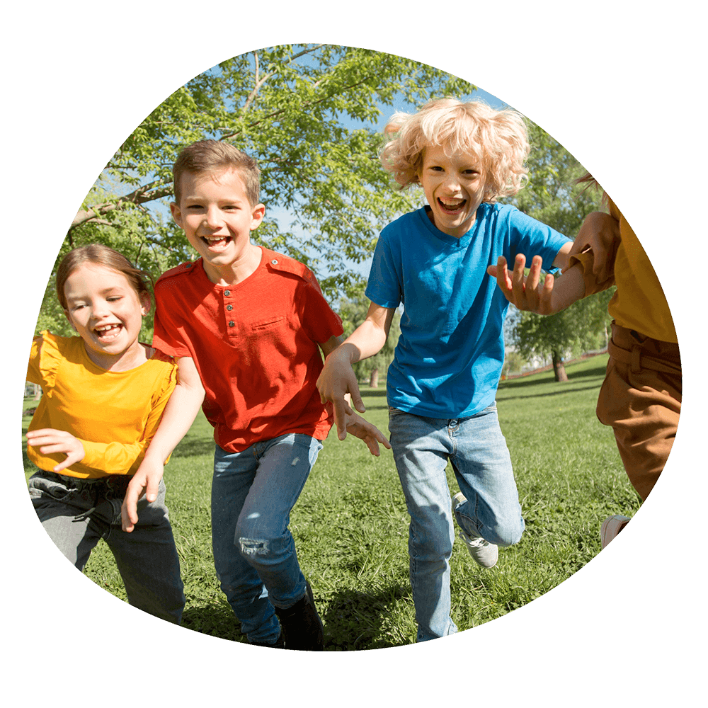 Tre bambini che corrono e ridono in un parco verde durante un'attività all'aperto del corso estivo Move Your Summer