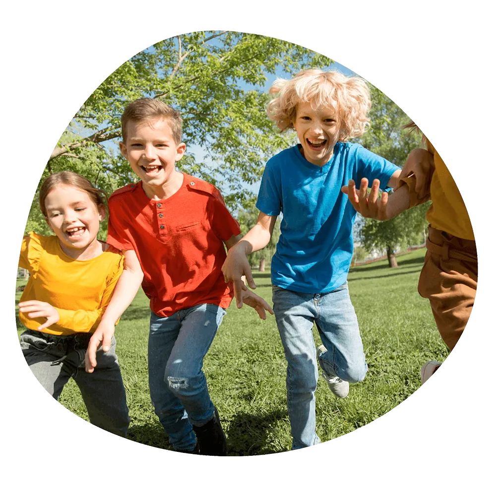 Tre bambini che corrono e ridono in un parco verde durante un'attività all'aperto del corso estivo Move Your Summer